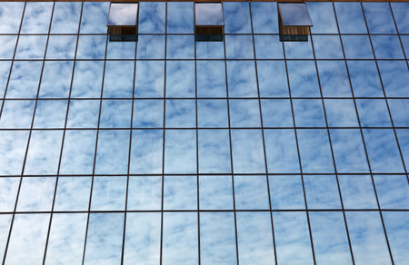 Cloudy blue sky reflection in glass of office business building with open windows, low angle view