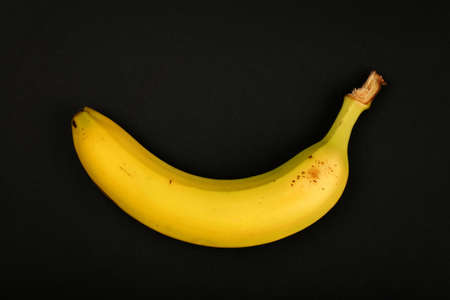 One fresh ripe yellow banana isolated on black paper background, close up, elevated top view, directly aboveの写真素材