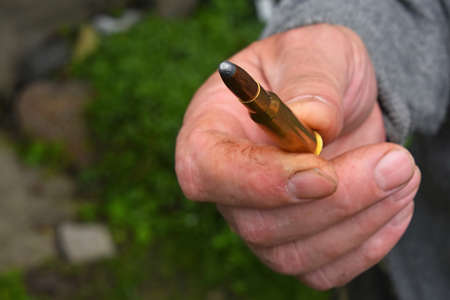 Old man hand holding and showing one 7.62 mm caliber ammunition bulletの写真素材