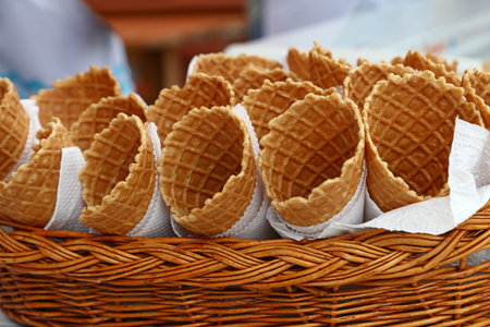 Several empty fresh wafer ice cream cone cornet cups with white paper napkins in wooden wicker...