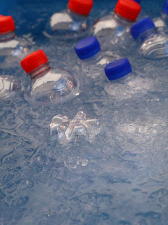PET plastic bottles of cold still and sparking drinking mineral water with blue and red caps float and chill down in ice and water on retail market display, close up, high angle viewの写真素材