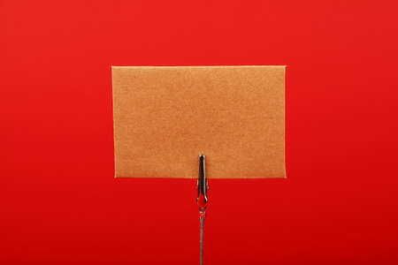 Blank brown kraft cardboard paper parchment sign with copy space on metal note holder over red background, front side viewの写真素材