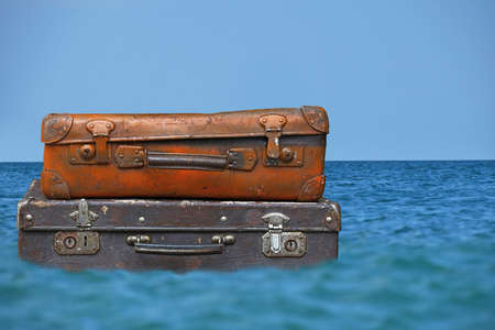 Stack of two old vintage antique grunge travel luggage brown leather suitcase trunks floating in blue sea water under clear sky, close up, low angle side viewの写真素材
