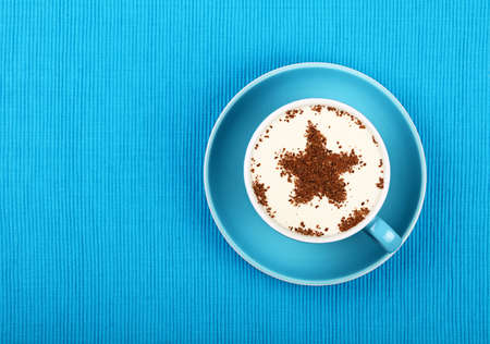 Close up one latte cappuccino coffee with star shaped chocolate milk topping in red cup with saucer over background of blue tablecloth, elevated top view, directly aboveの写真素材