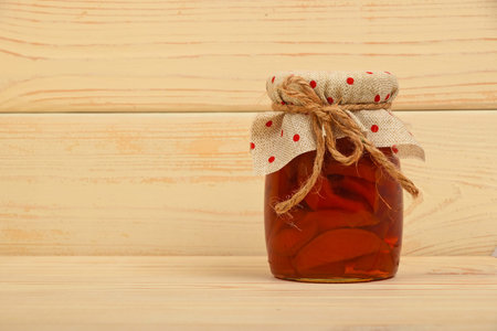 Close up of one glass jar of homemade quince jam with textile top decoration and twine bow over white beige painted vintage wooden planks background, low angle side viewの写真素材