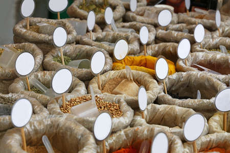 Close up many canvas bags of assorted spices with copy space of blank price tags on retail display of market stall, high angle viewの写真素材
