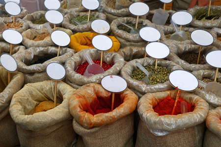 Close up canvas bags of assorted spices with copy space of blank price tags on retail display of market stall, high angle viewの写真素材