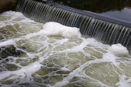 Dirty polluted river water running, falling from jetty mole rift and foaming, high angle diagonal...