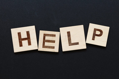 Close up word HELP on wooden letter signs over black board backgroundの写真素材
