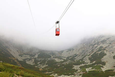 Red mountain cableway car lift in clouds and fog, low angle viewの写真素材