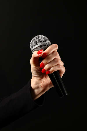 Woman hand with red nails holding microphone isolated on black backgroundの写真素材
