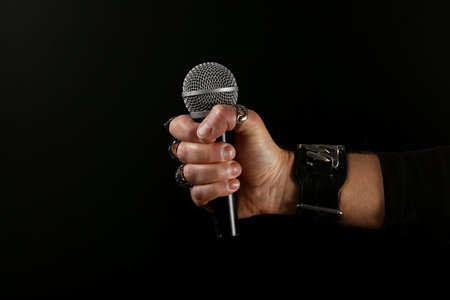 Close up man hand with metal rings and bracelet holding microphone over black background, side viewの写真素材