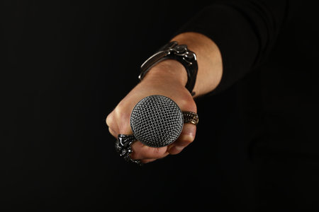 Close up man hand with metal rings and bracelet holding microphone over black background, side view