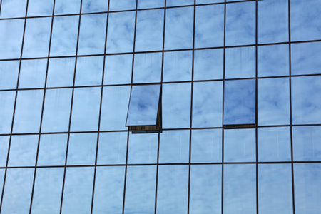 Cloudy blue sky reflection in glass of office business building with open windows, low angle viewの写真素材