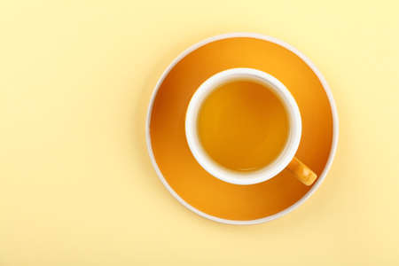 Close up one full yellow cup of green oolong or herbal tea on saucer over pastel paper background, elevated top view, directly aboveの写真素材