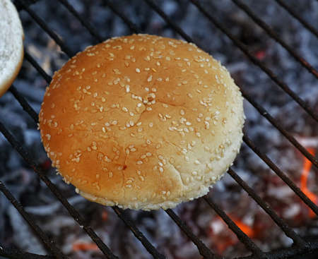 Close up sesame bun for hamburger burger cooked on fire barbecue grill with smoke and flame, high angle viewの写真素材
