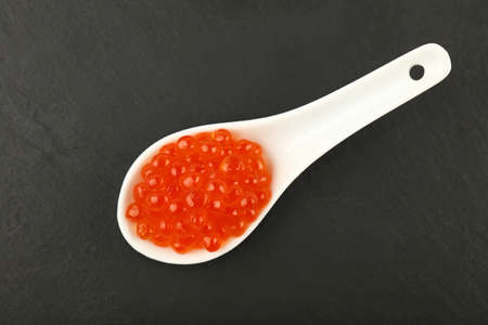 Close up one portion of salmon fish red caviar in white spoon on background of black slate kitchen board, elevated top view, directly aboveの写真素材