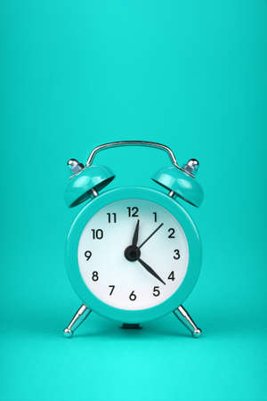 Close up one small teal blue metal twin bell retro alarm clock over aqua turquoise paper background with copy space, low angle front viewの写真素材