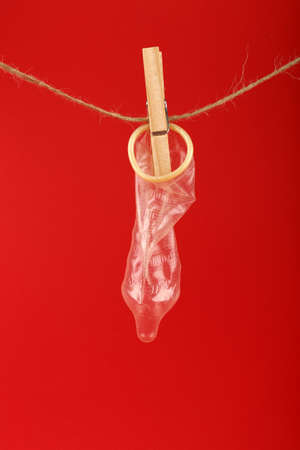 Close up one condom hanging on twine washing line with wooden clothespin over red background with copy space, low angle side viewの写真素材