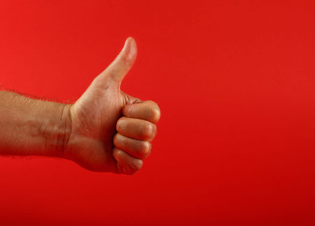Man hand shoving thumb up ok good gesture over red background, side view