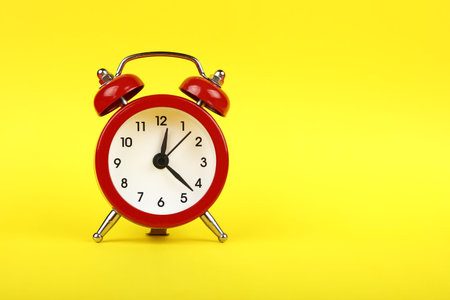 Close up one small red metal twin bell retro alarm clock over yellow paper background with copy...