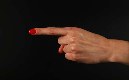 Woman hand with red nails showing direction or pointing with index finger gesture isolated on black background, side viewの写真素材