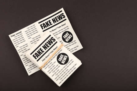 Close up stack of FAKE NEWS newspapers over black paper background with copy space, elevated top view, directly aboveの写真素材