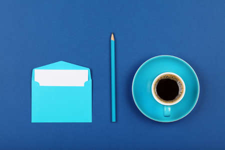 One open blank pastel blue envelope with white paper, black coffee cup and wooden pencil over dark indigo blue background, flat lay, directly aboveの写真素材