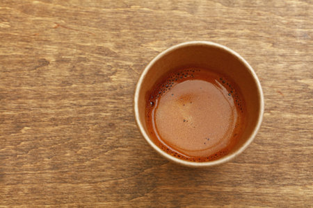 Close up one disposable brown paper cup full of espresso coffee on wooden table, elevated top view, directly aboveの写真素材