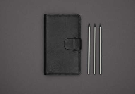 Close up one closed black leather cover notebook and pencils over grey paper background, flat lay, directly aboveの写真素材