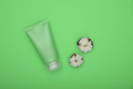 Close up one bottle of shower gel, shampoo or body care beauty product and white cotton flower over green background, elevated top view, directly aboveの写真素材