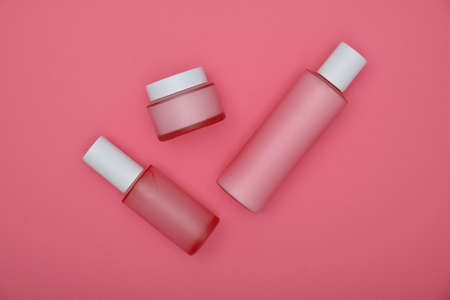 Close up set of three cosmetic skin care cream, lotion and tonic bottles over pink background, elevated top view, directly aboveの写真素材