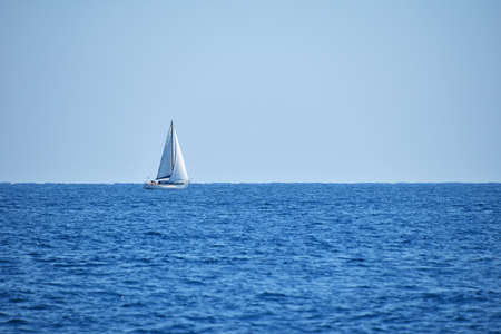 Tranquil seascape with calm sea water ripples and waves and sail yacht under clear day blue sky, high angle viewの写真素材