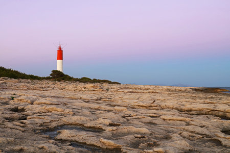 Rocky sea coast landscape with lighthouse over clear pink sunset sky, low angle viewの写真素材