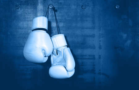 Close up pair of clasic white leather boxing gloves hanging over dark blue wall with copy spaceの写真素材