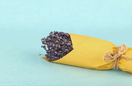 Close up bouquet of dried lavender flowers wrapped in yellow paper on blue tablecloth, high angle viewの写真素材