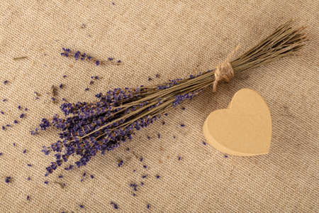 Close up bouquet of dried lavender flowers and small heart shaped gift box on brown canvas tablecloth, elevated top view, directly aboveの写真素材