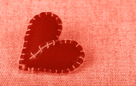 Close up coral pink color toned Valentine Day template, one handmade felt craft stitched toy heart...