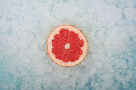 Close up one fresh juicy pink grapefruit slice over background of crushed ice, elevated high angle view, directly aboveの写真素材