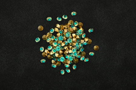 Close up heap of teal blue rhinestone crystals over black leather background, elevated top view,...