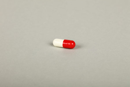 Close up one red and white gel cap pill of medicine over grey background with copy space, high angle...