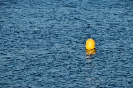 Turquoise blue sea water surface with ripples and waves, yellow floating buoy, high angle viewの写真素材