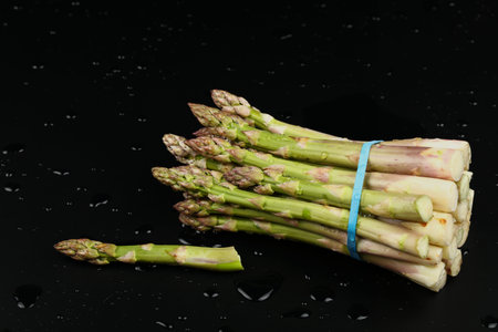 Close up bunch of washed fresh green asparagus on black table with drops of water, high angle viewの写真素材
