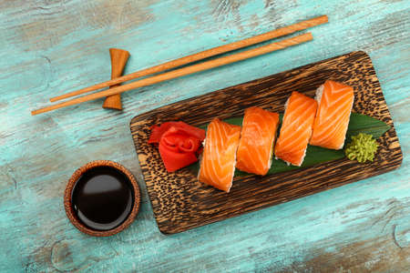 Close up one set of six Philadelphia sushi rolls with raw salmon served on palm wood plate on blue table, elevated top view, directly aboveの写真素材