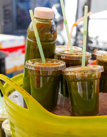 Close up fresh green fruit and vegetable juice in plastic bottles and glasses with drinking straws at retail display, low angle side viewの写真素材