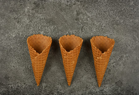 Close up three empty wafer ice cream cones on gray table, elevated top view, directly above