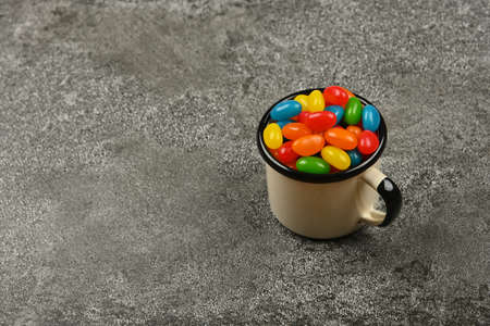 Close up multicolor jelly beans candies in vintage white metal mug on grunge gray table surface, high angle viewの写真素材