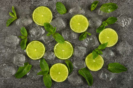 Close up flat lay of lime slices, fresh green mint leaves and ice cubes on grunge gray stone table surface, elevated top view, directly aboveの写真素材