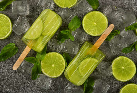 Close up two frozen fruit juice  with fresh lime slices, green mint leaves and ice cubes on gray table surface, elevated top view, directly aboveの写真素材
