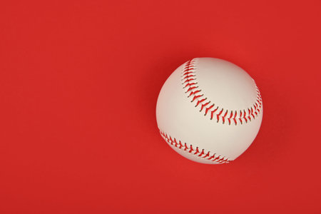 Close up one new baseball ball with red stitch over vivid red background, elevated top view,...